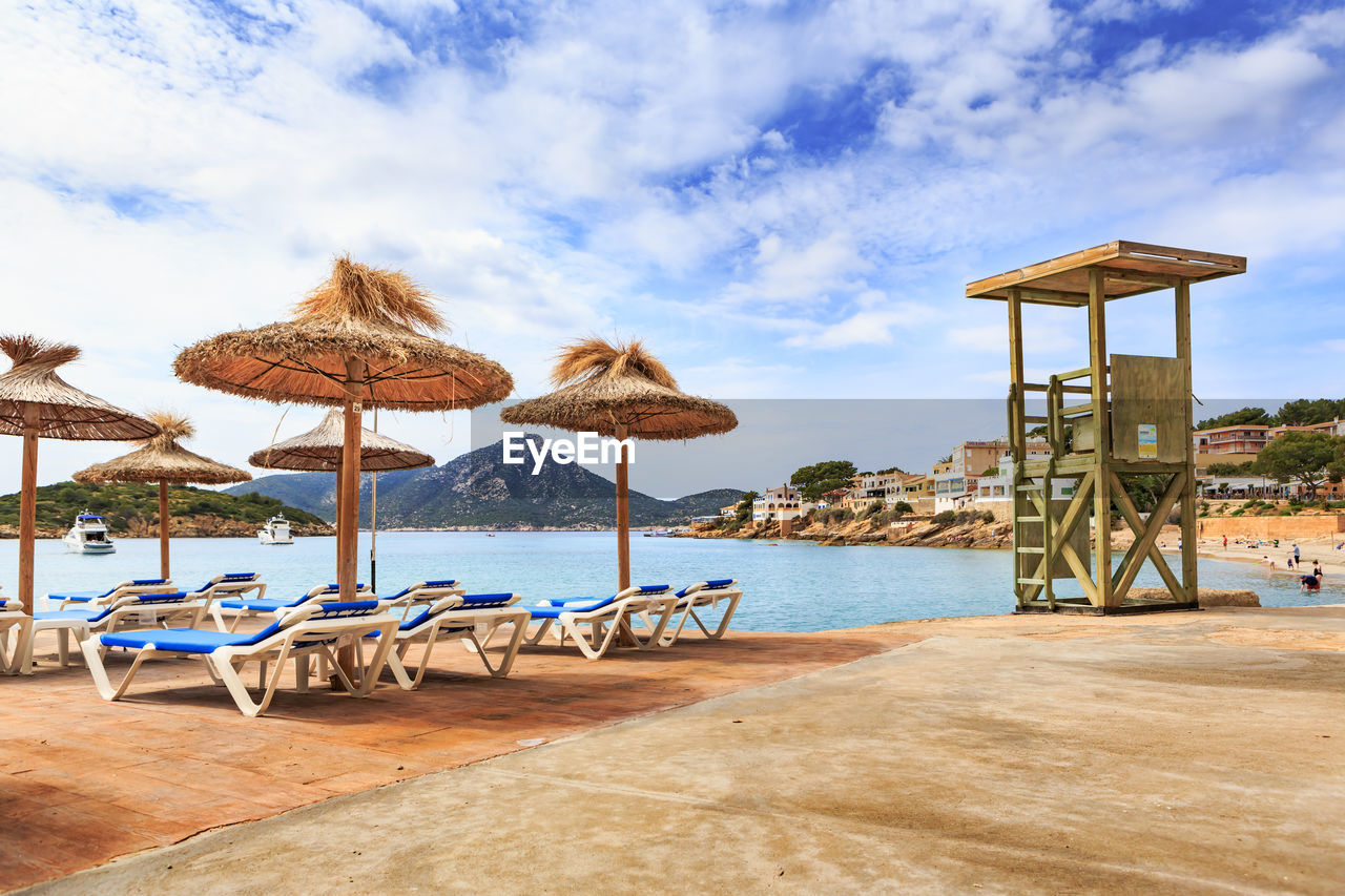 Deck chairs with umbrellas at beach against cloudy sky