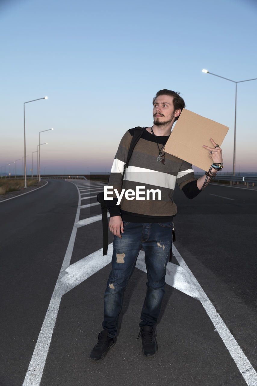 Man with cardboard standing on road against sky