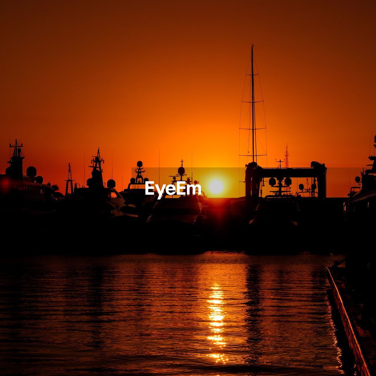 SILHOUETTE BOATS MOORED AT HARBOR AGAINST ORANGE SKY