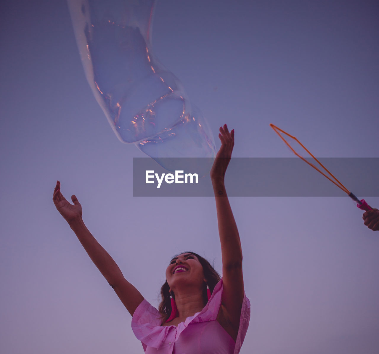 Low angle view of cheerful woman playing with bubble against sky during sunset
