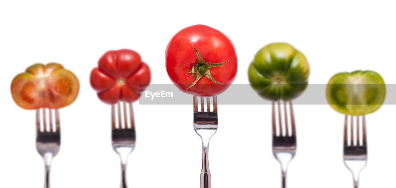 Close-up of tomatoes on forks against white background