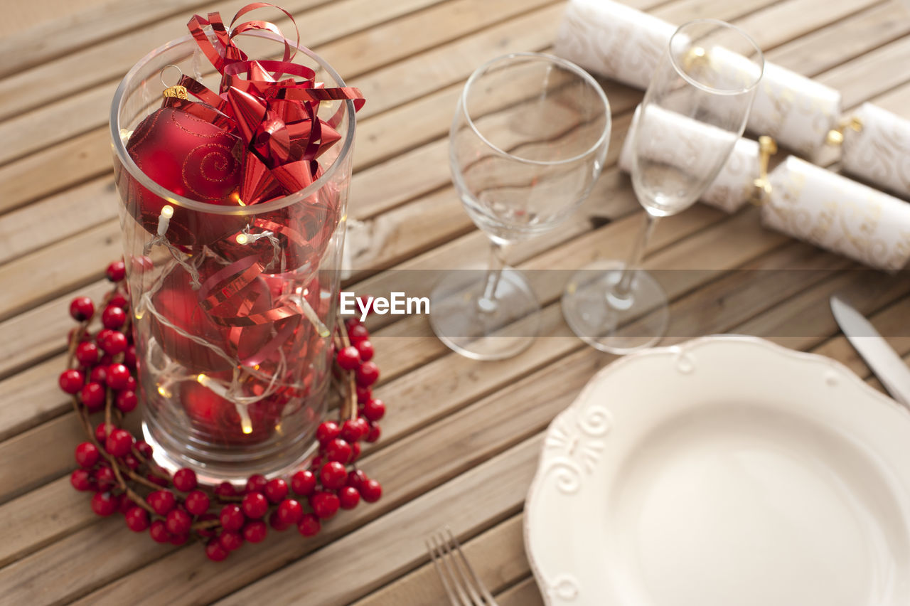 Christmas table setting with red decorations and berries on a slatted wood table ready to celebrate