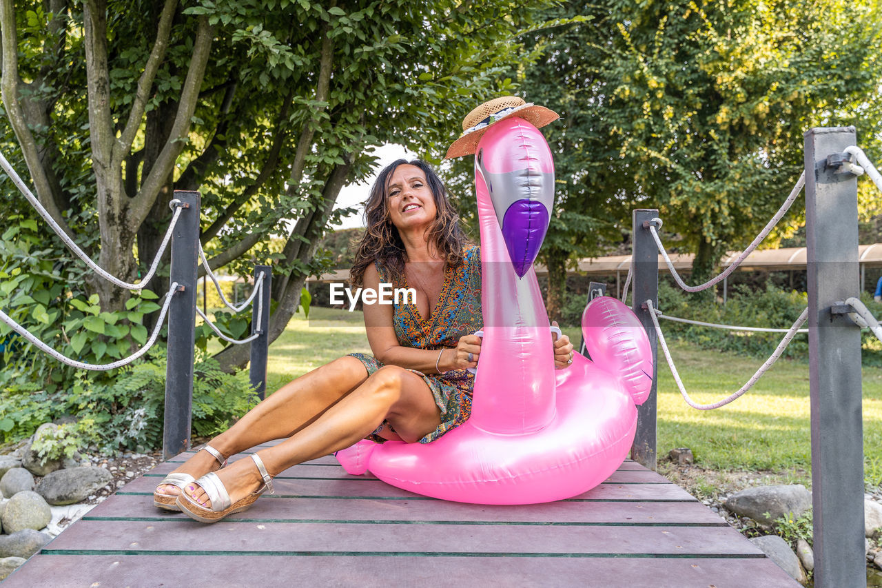 Portrait of beautiful middle aged woman sitting on pink flamingo inflatable toy