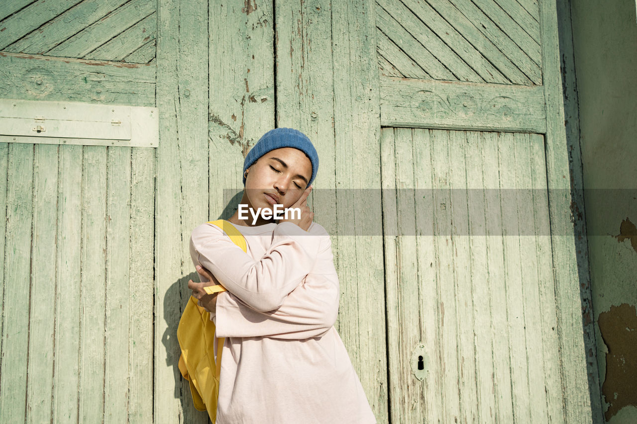 Young woman with eyes closed standing in front of door