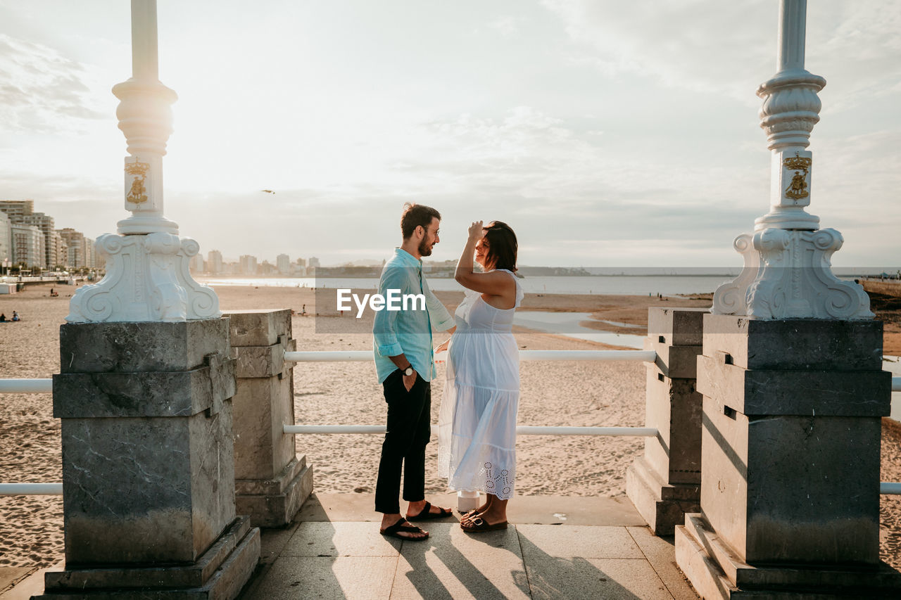 Full length of couple embracing while standing on beach against sky