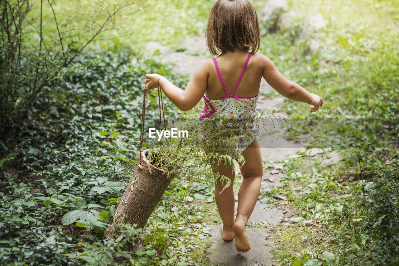 Rear view of girl carrying wooden basket with plants