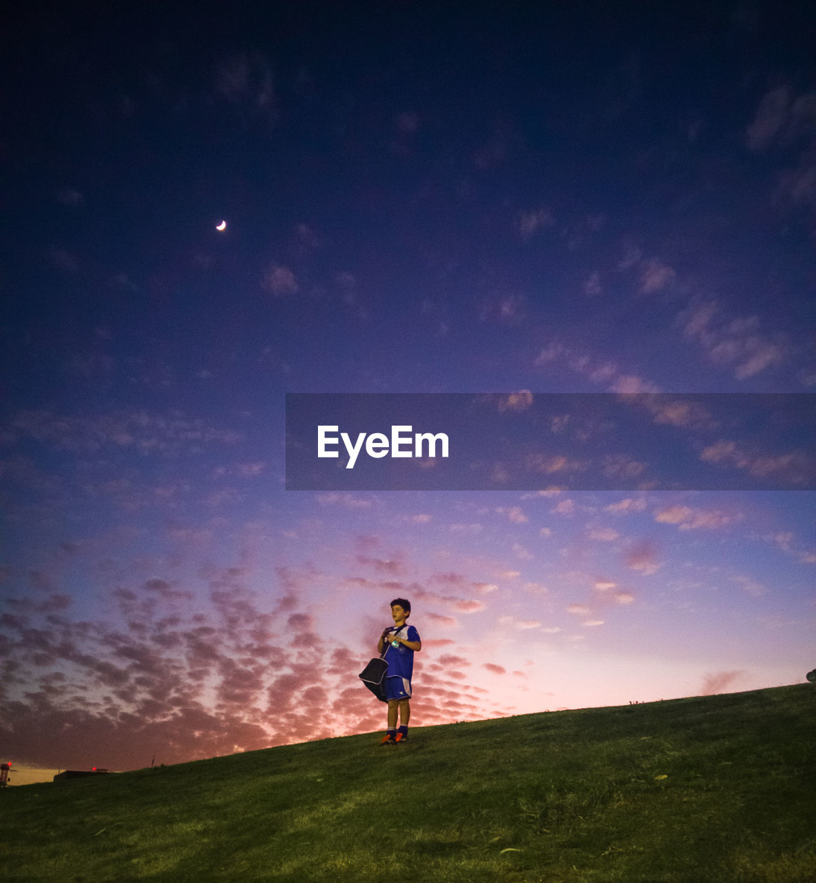 Boy in sports clothing on hill at sunset