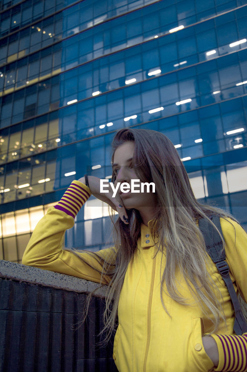 Low angle view of thoughtful young woman standing against building