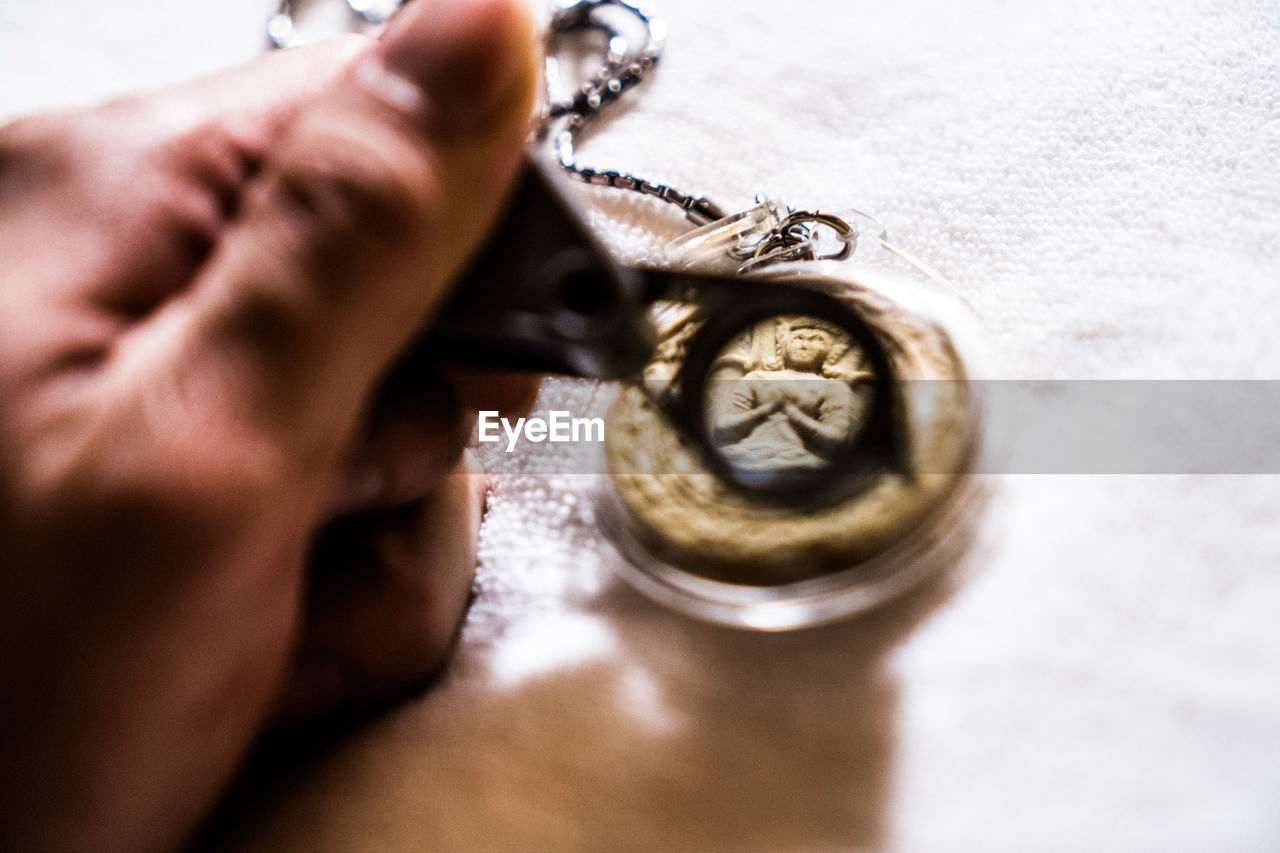 Close-up of human hand holding magnifying glass against necklace