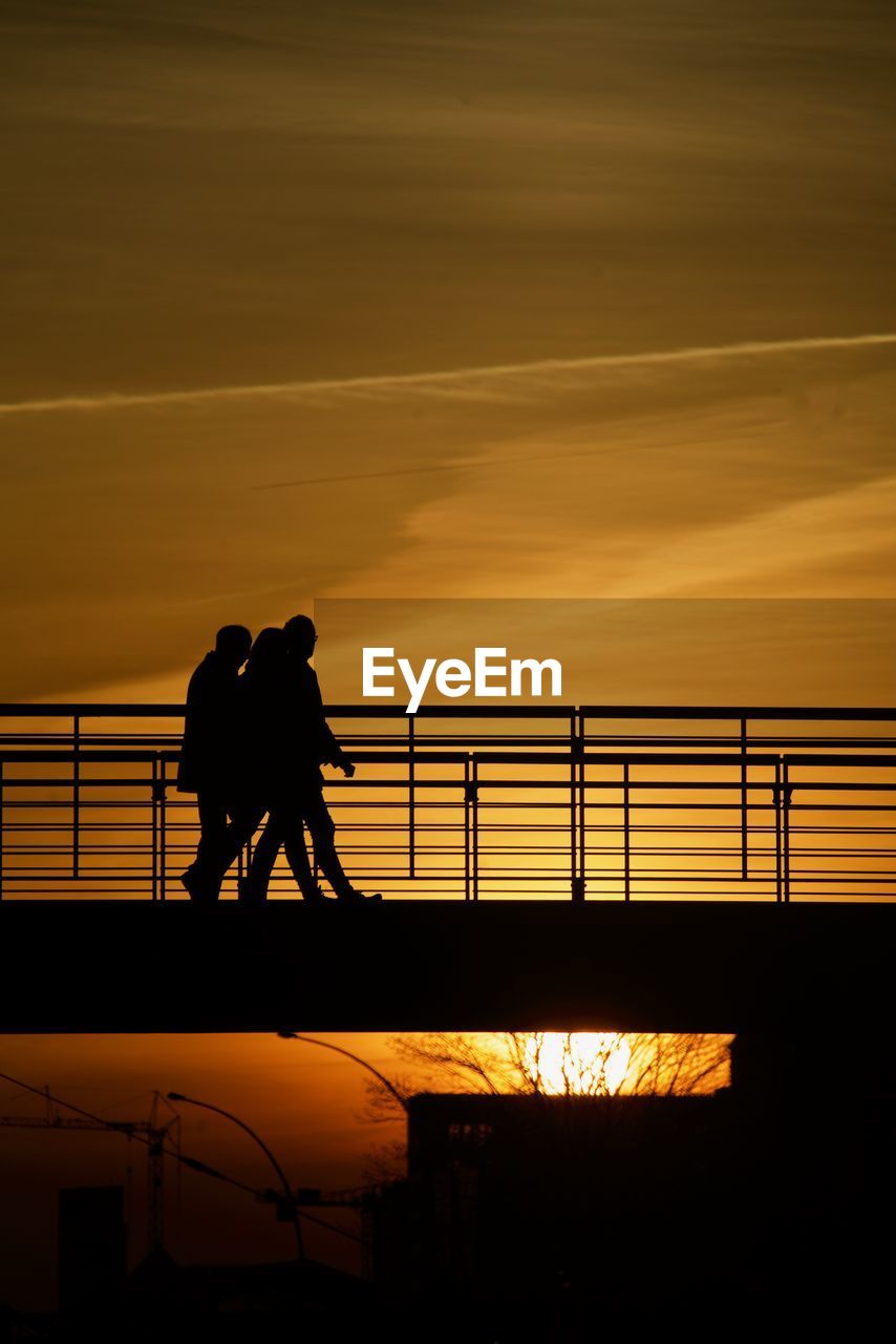 SILHOUETTE COUPLE STANDING AGAINST RAILING DURING SUNSET