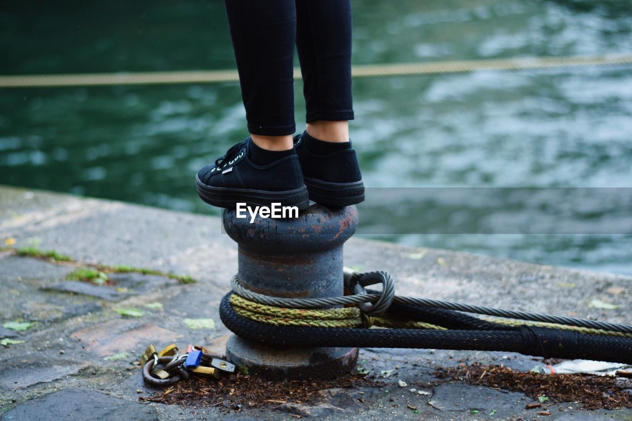 Low section of man standing on bollard at harbor