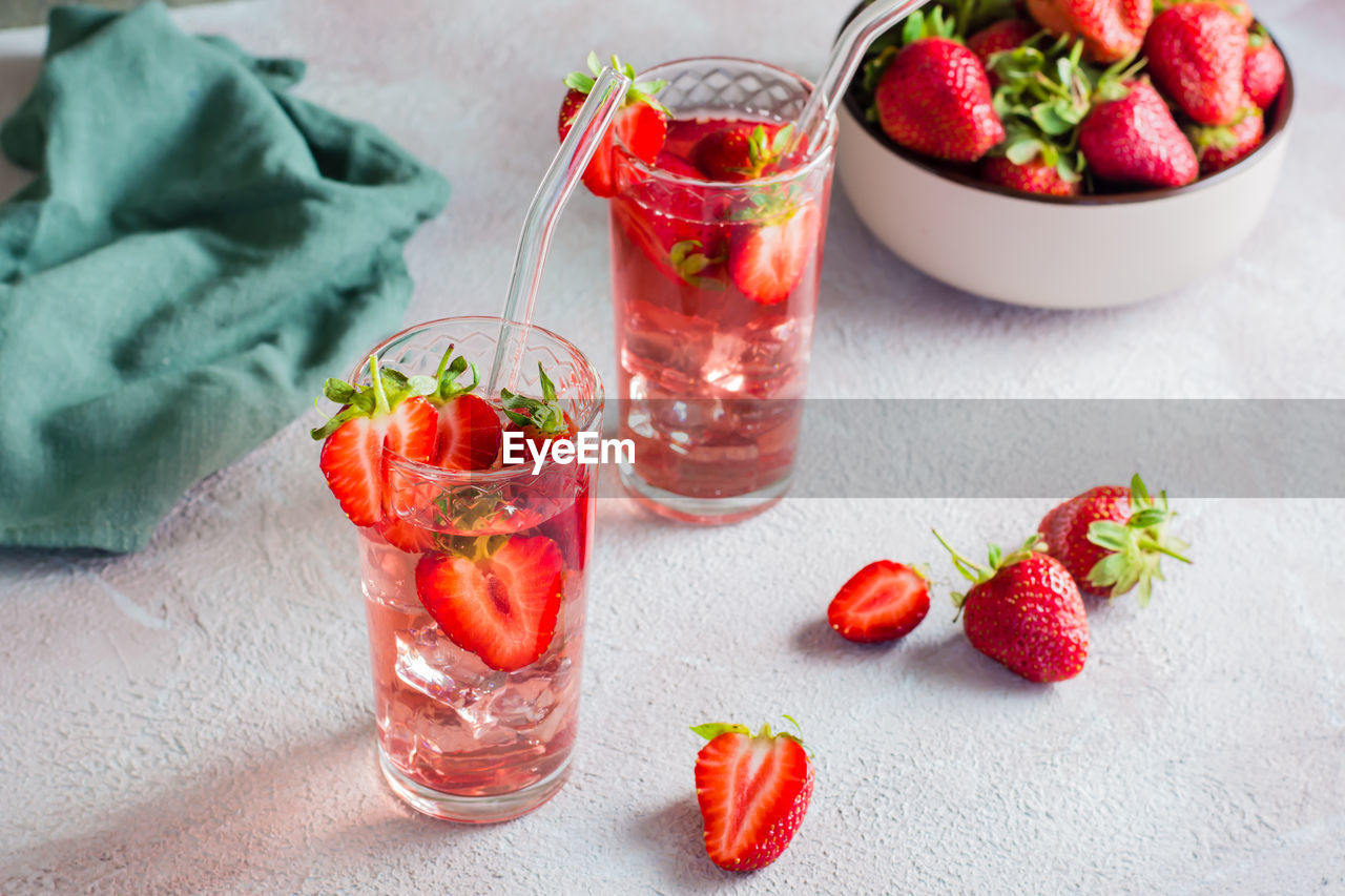 Two glasses with a strawberry cocktail and a bowl of berries on the table. homemade drinks