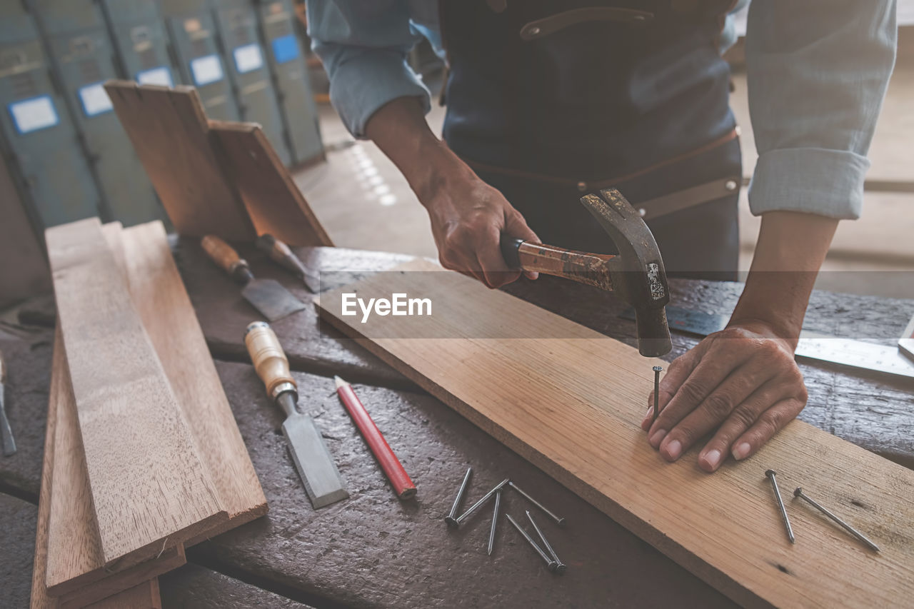 Midsection of carpenter hammering nail in plank at workshop