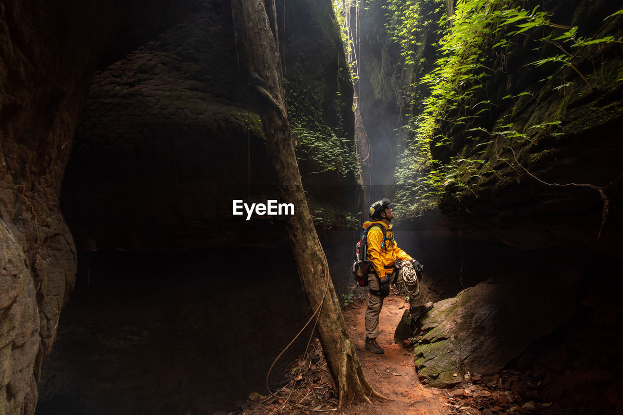 MAN STANDING ON ROCK AGAINST TREES