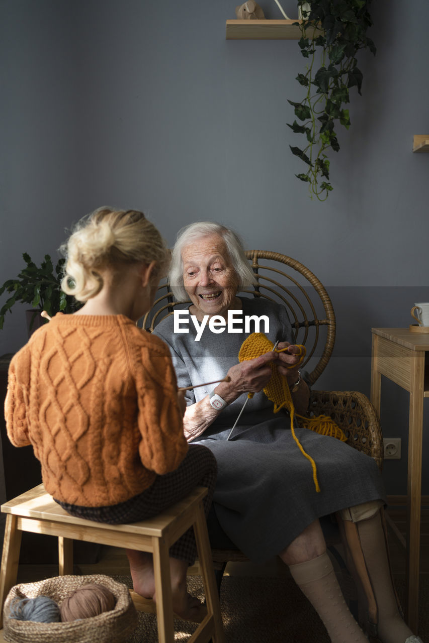 Happy grandmother teaching granddaughter to knit at home