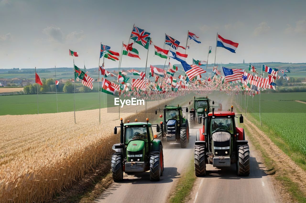 transportation, mode of transportation, landscape, nature, vehicle, land, sky, environment, flag, land vehicle, car, tractor, road, day, motion, rural scene, sports, outdoors, agricultural machinery, on the move, agriculture, travel, field, driving, in a row, race track, plant, cloud