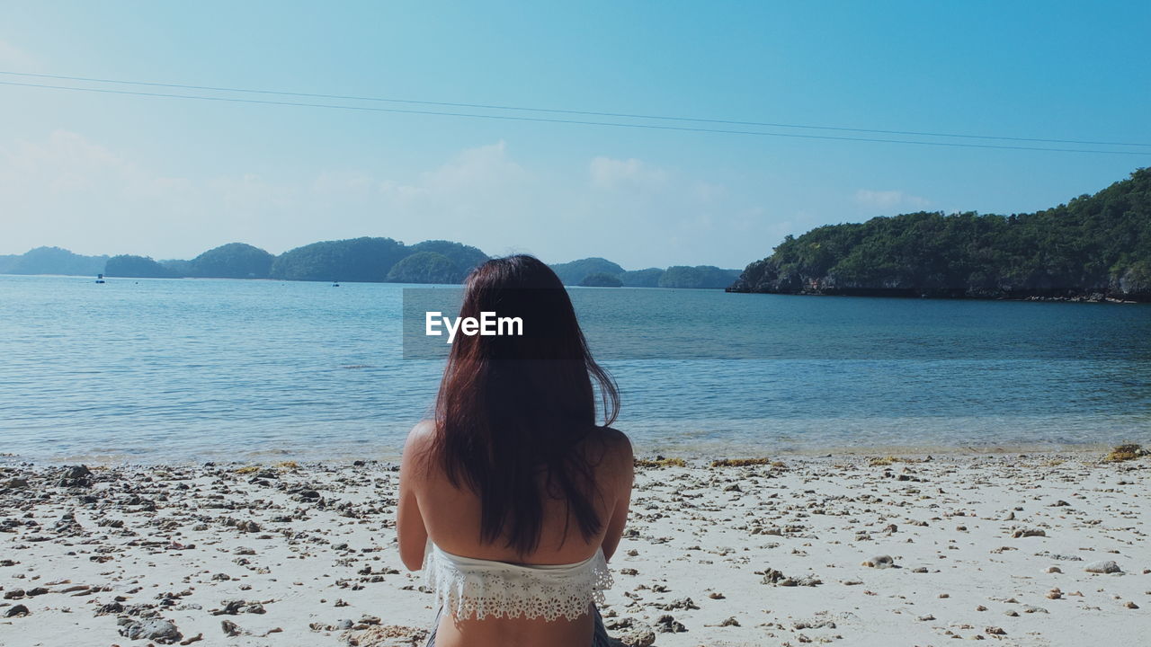 Rear view of woman at beach against sky