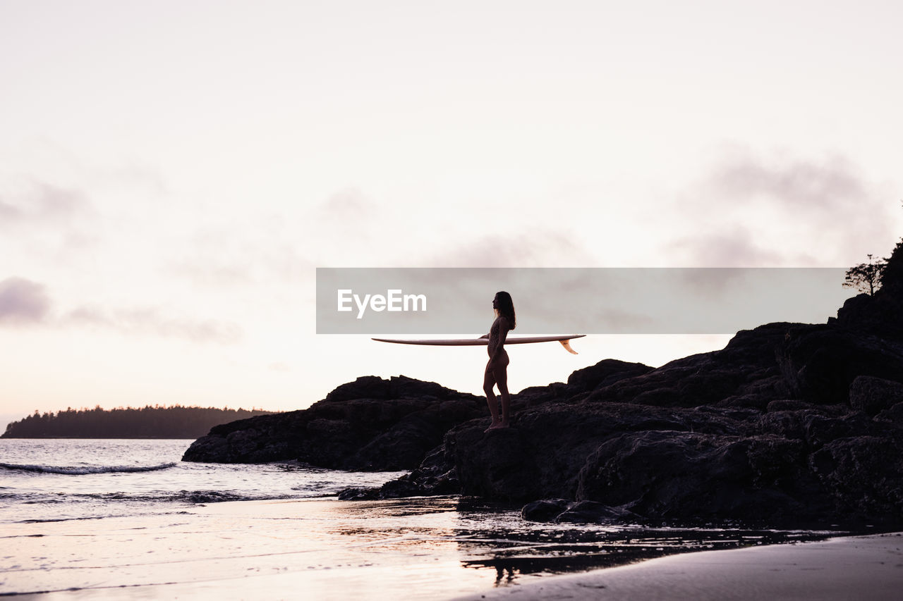 Beautiful, fit woman with surfboard on beach in tofino