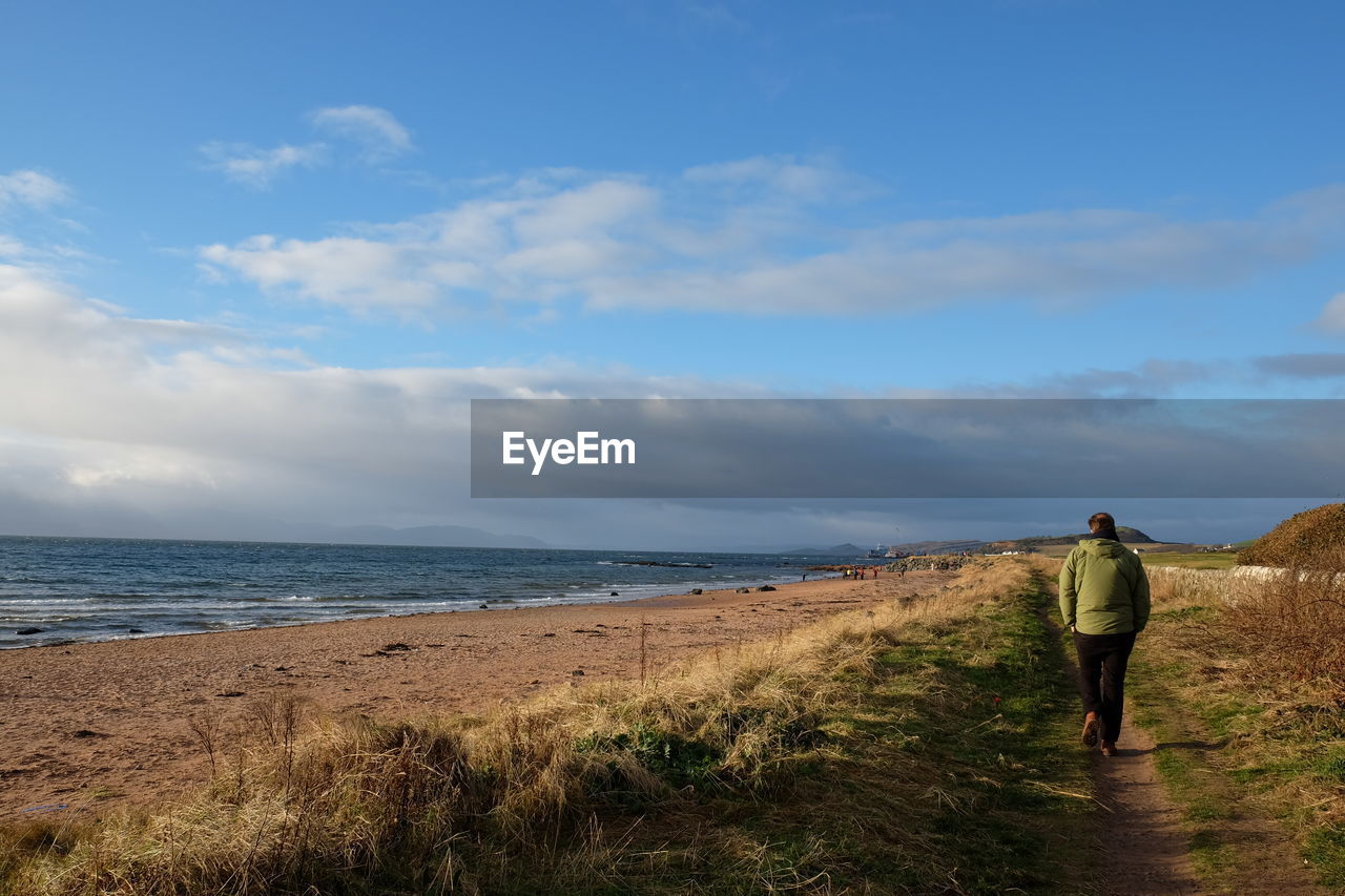 Rear view of woman walking at beach against sky