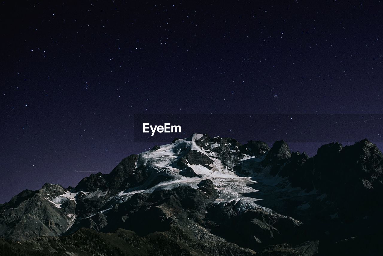 Low angle view of mountains against star field at night