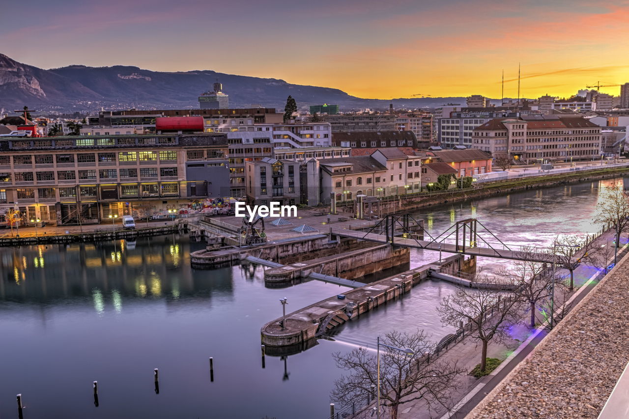 Bridge over river in city against sky during sunset