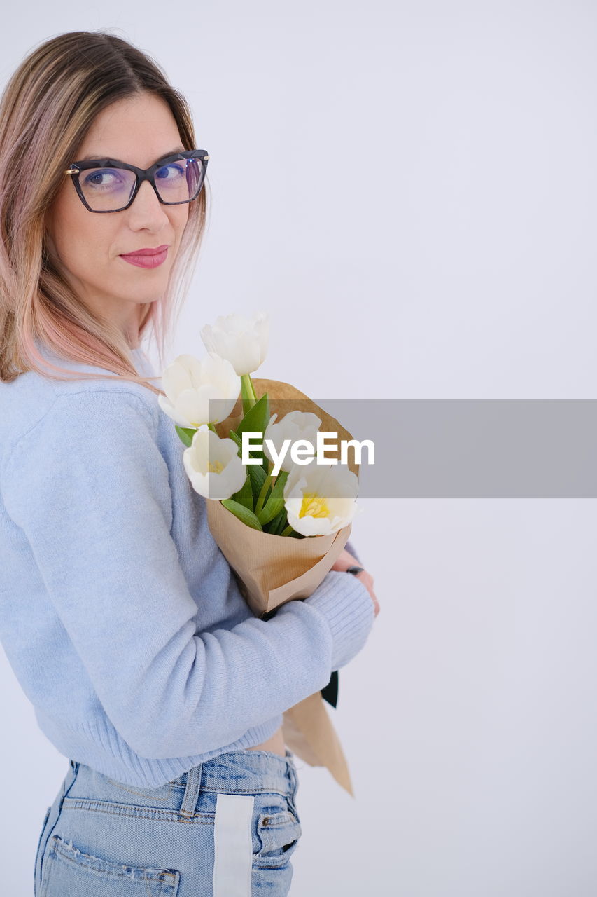 flower, women, adult, studio shot, one person, indoors, flowering plant, young adult, female, glasses, emotion, copy space, portrait, plant, clothing, rose, holding, eyeglasses, fun, person, blond hair, lifestyles, freshness, hand, casual clothing, happiness, smiling, nature, positive emotion, human hair, human face
