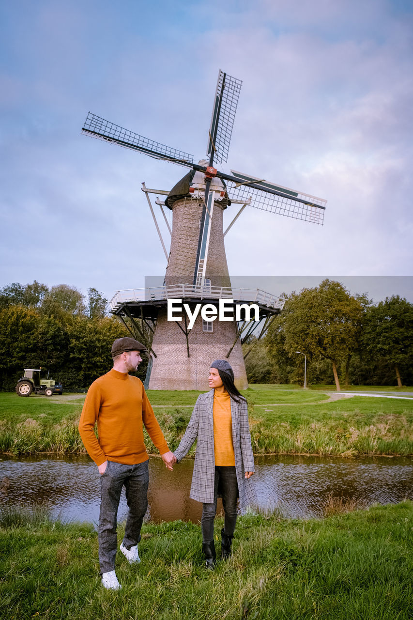 Couple holding hands while standing on land against sky