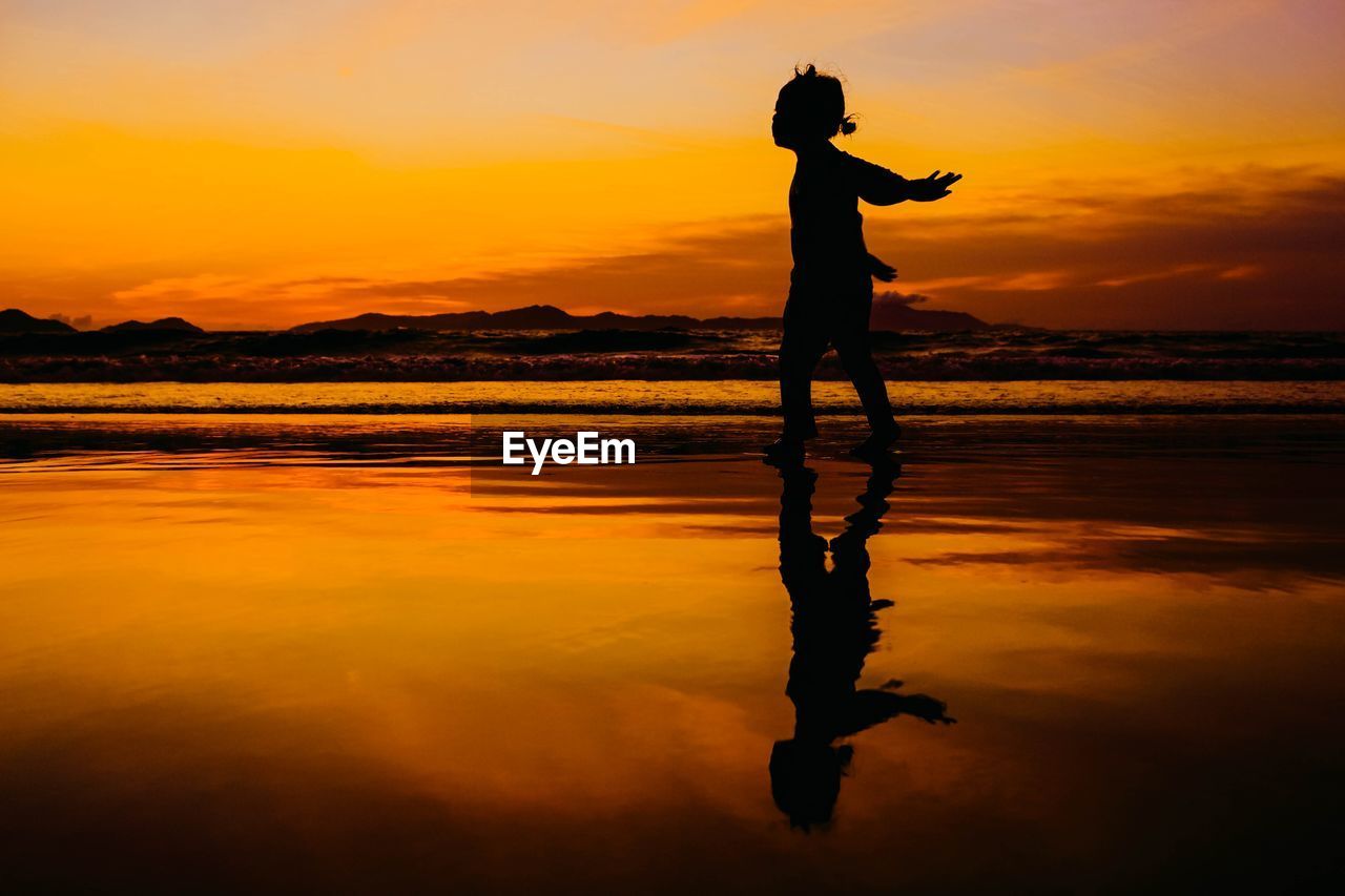 Silhouette girl walking on beach against sky during sunset