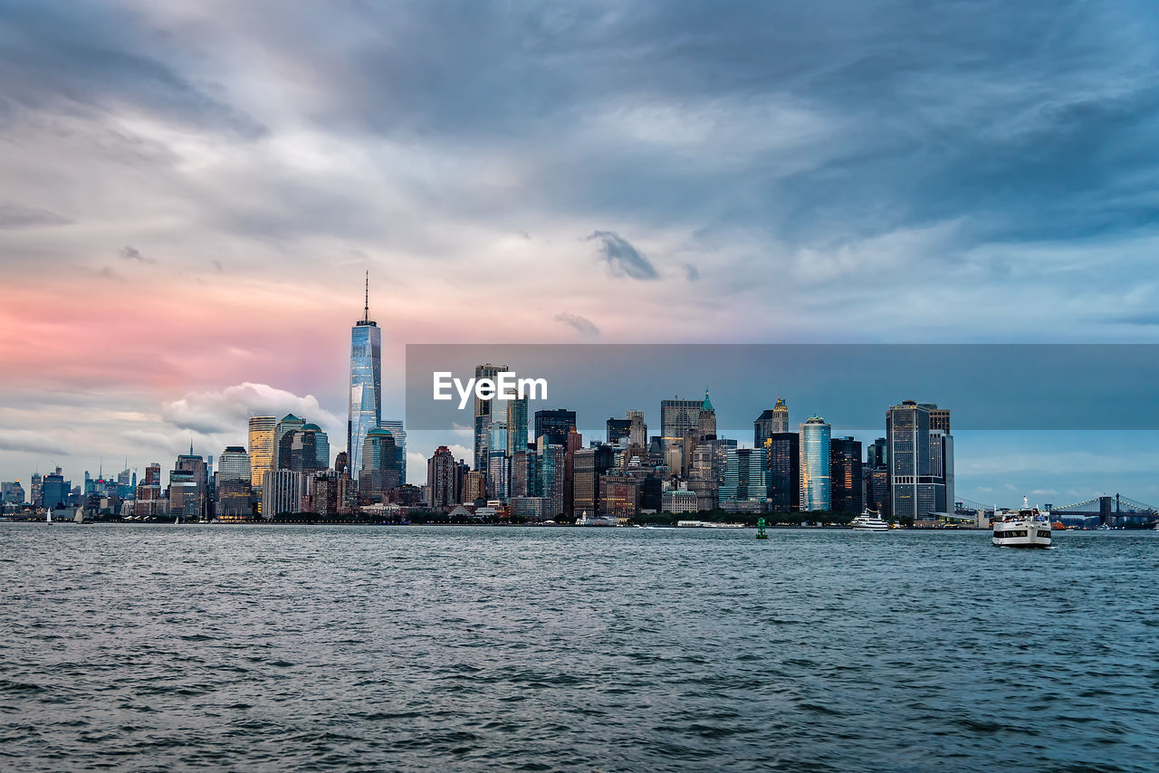 Sea and buildings in city against cloudy sky