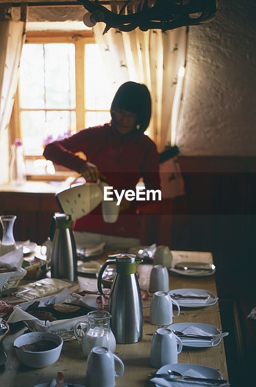 Woman pouring drink by table in cup