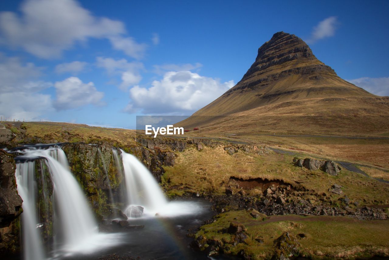 SCENIC VIEW OF WATERFALL BY MOUNTAIN AGAINST SKY