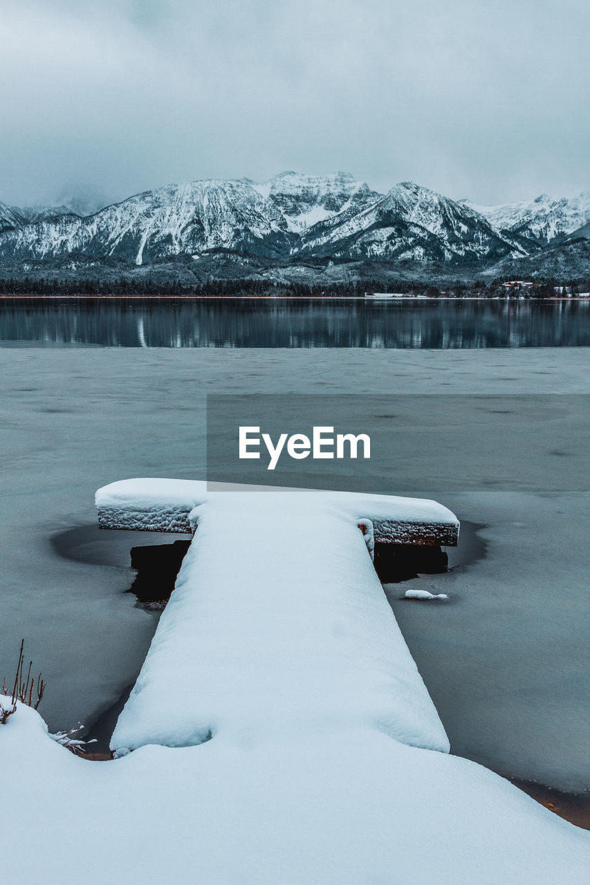 The hopfensee with the allgäu alps in winter. germany. in the foreground snow-covered jetty.