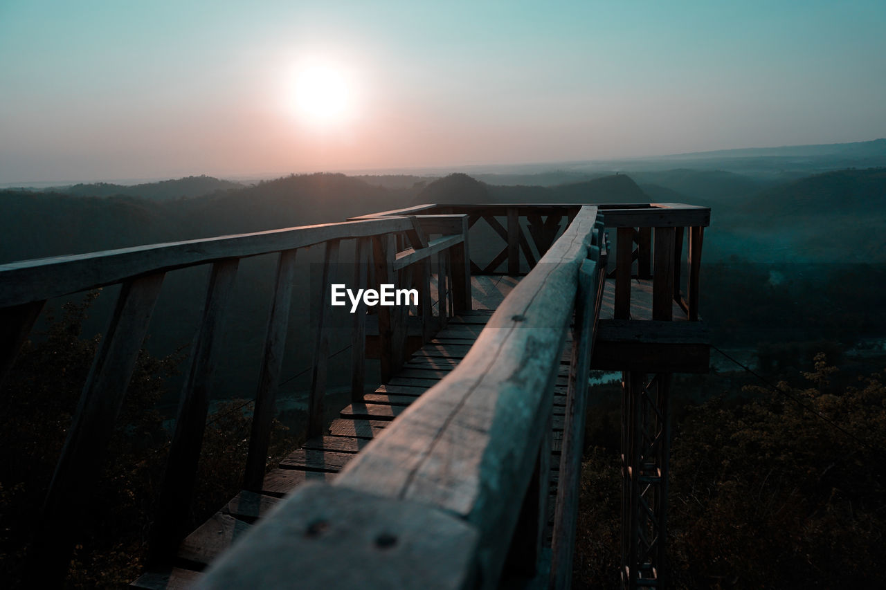 Footbridge against landscape and sky during sunset