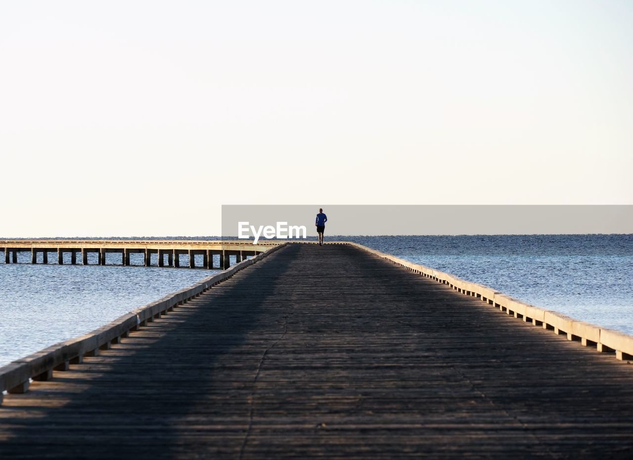 Man standing on pier over sea against clear sky