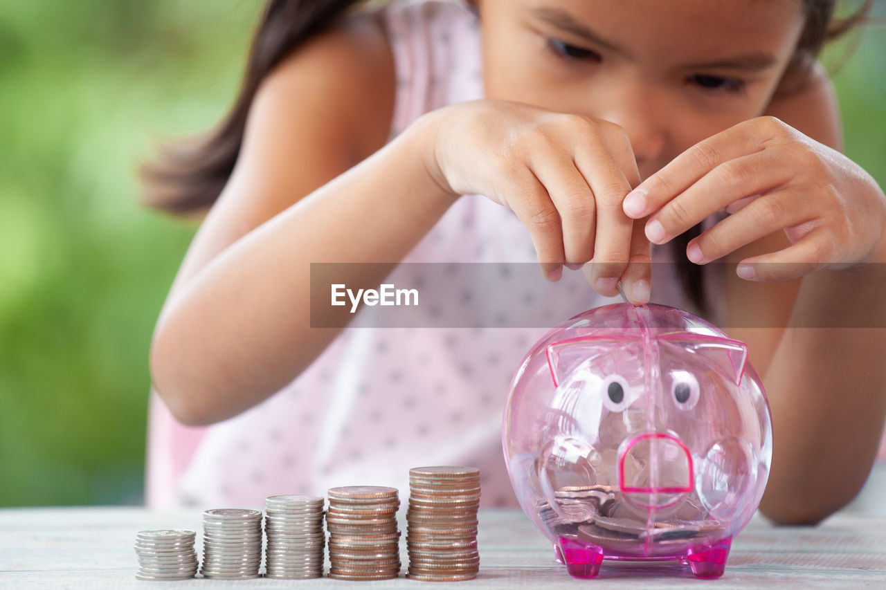 Girl putting coin in piggy bank at table