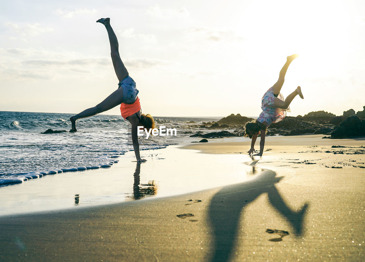 People doing handstand at beach against sky