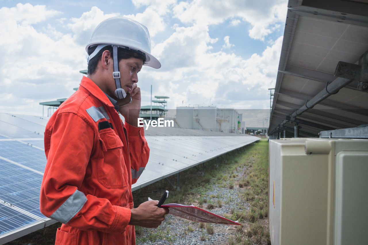 Side view of worker talking on phone while standing by solar panel