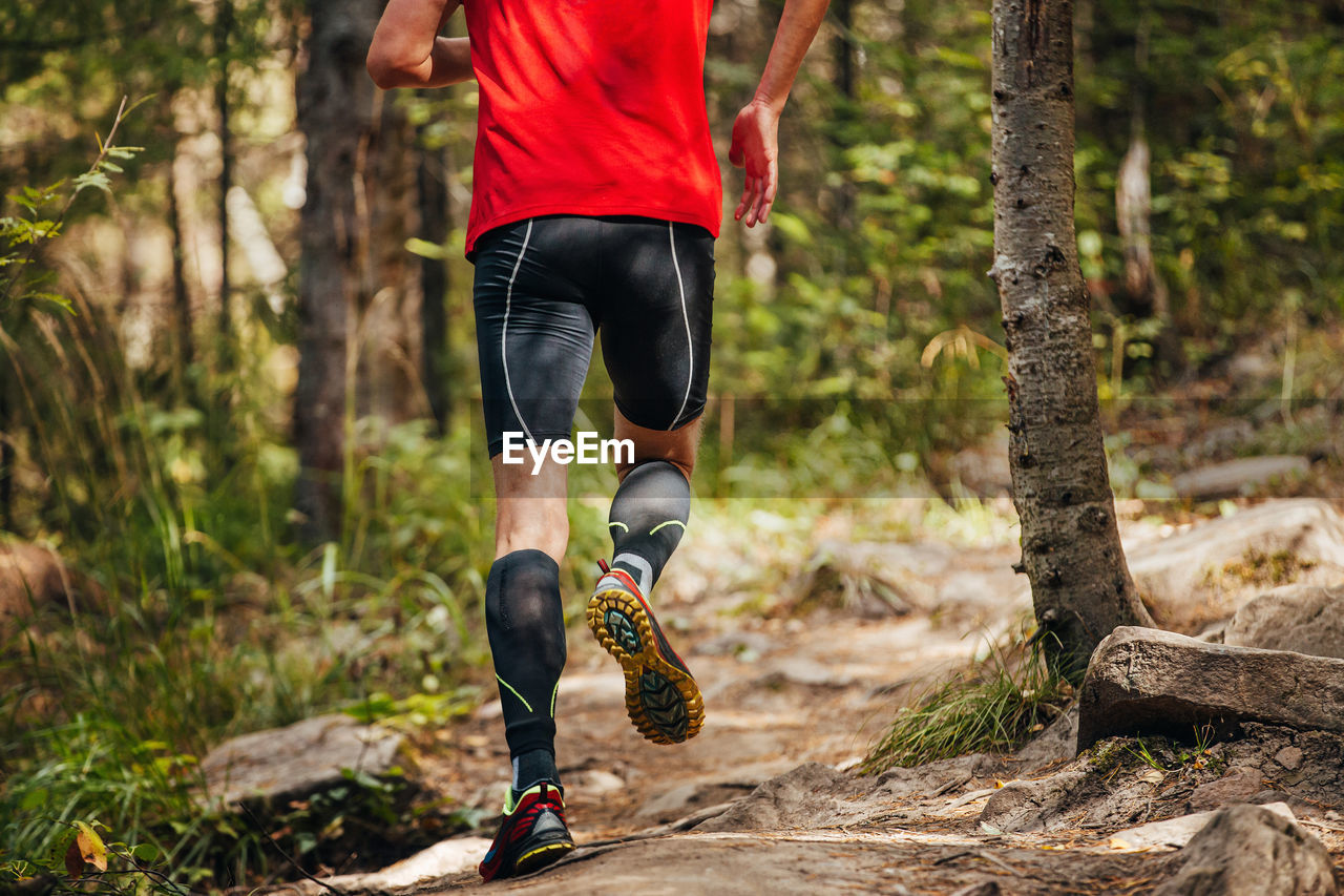 Male runner in compression calf sleeve running forest trail