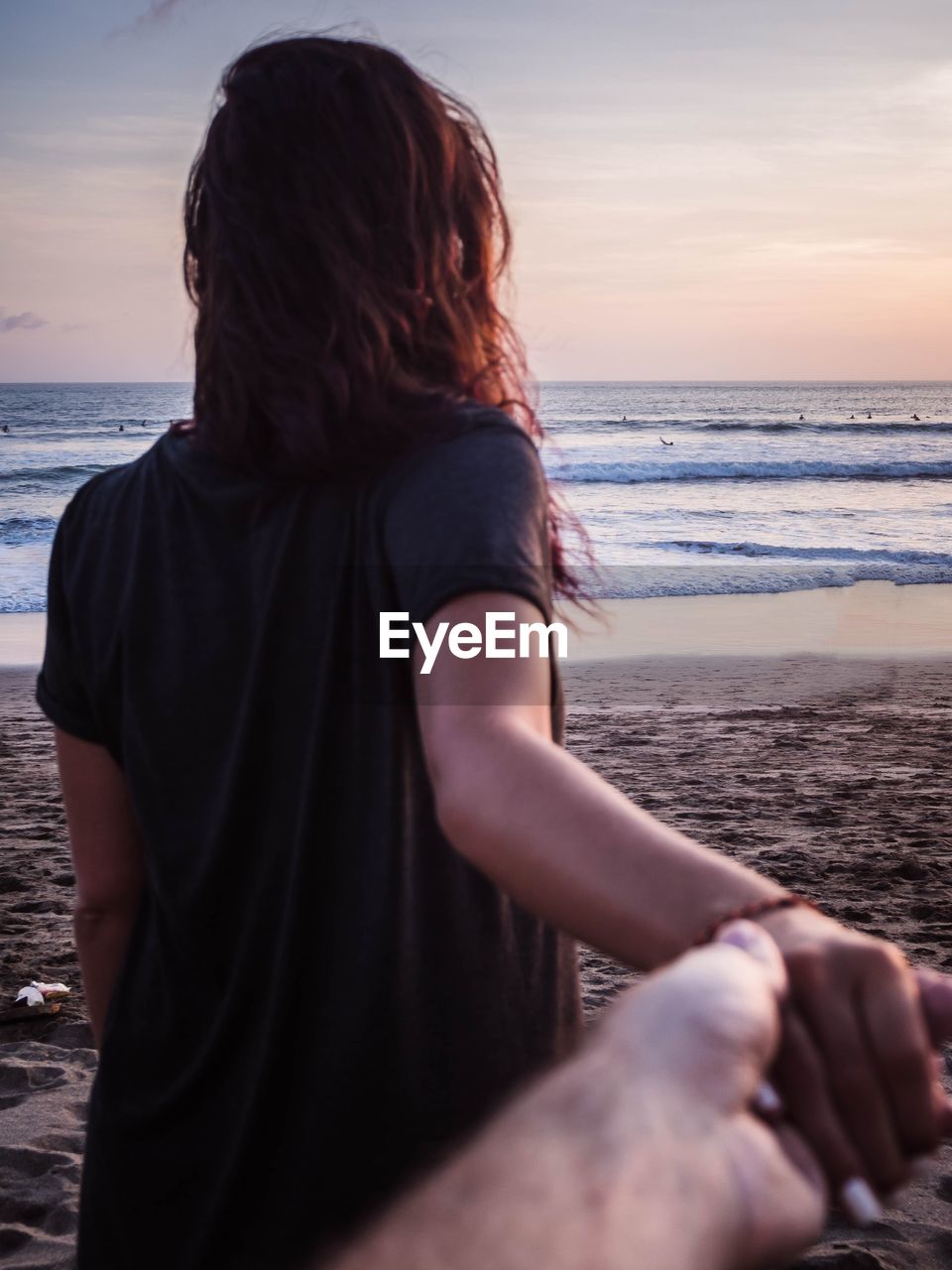 Cropped image of woman and man holding hands at beach