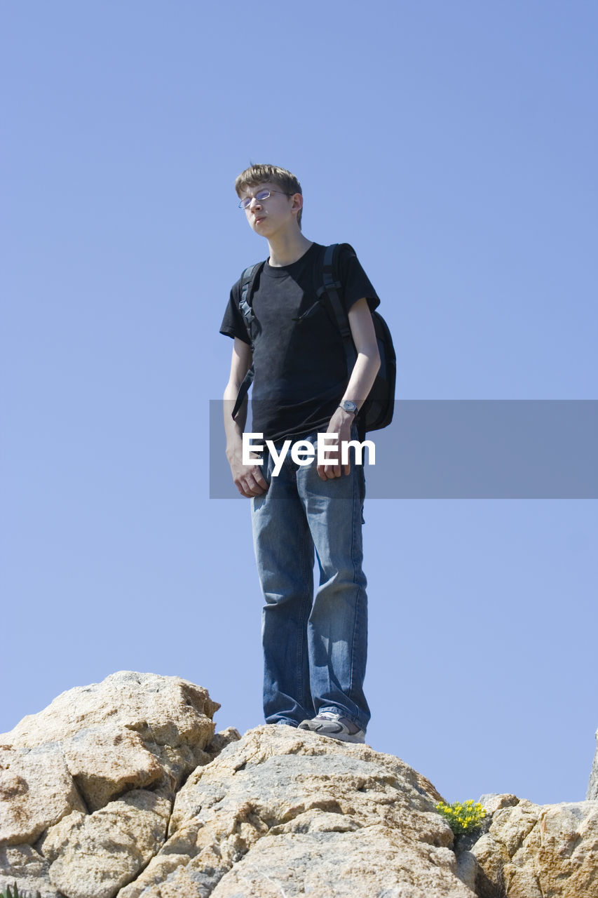 LOW ANGLE VIEW OF MAN STANDING ON ROCK