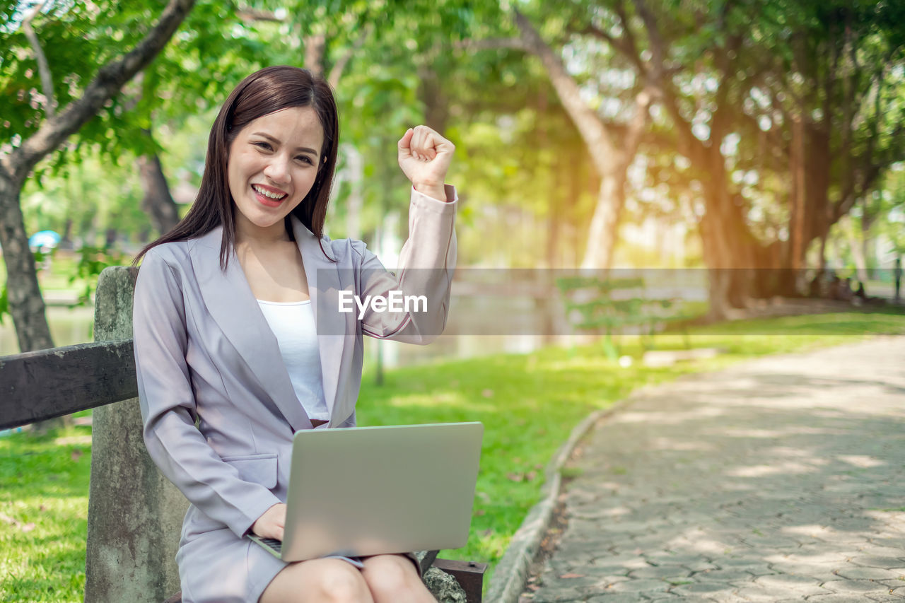 Portrait of smiling businesswoman gesturing while using laptop at park
