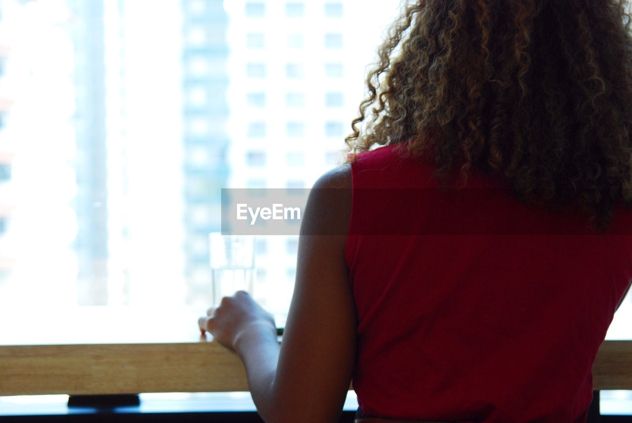 REAR VIEW OF WOMAN SITTING ON TABLE AT HOME
