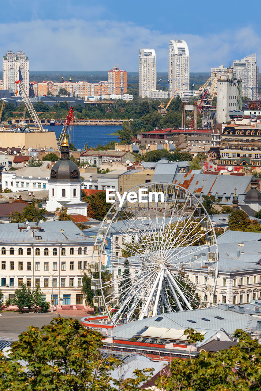 Summer cityscape of the old podil district of kyiv, with a ferris wheel and a bell tower.