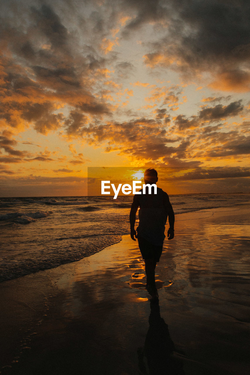 Silhouette man standing at beach against sky during sunset