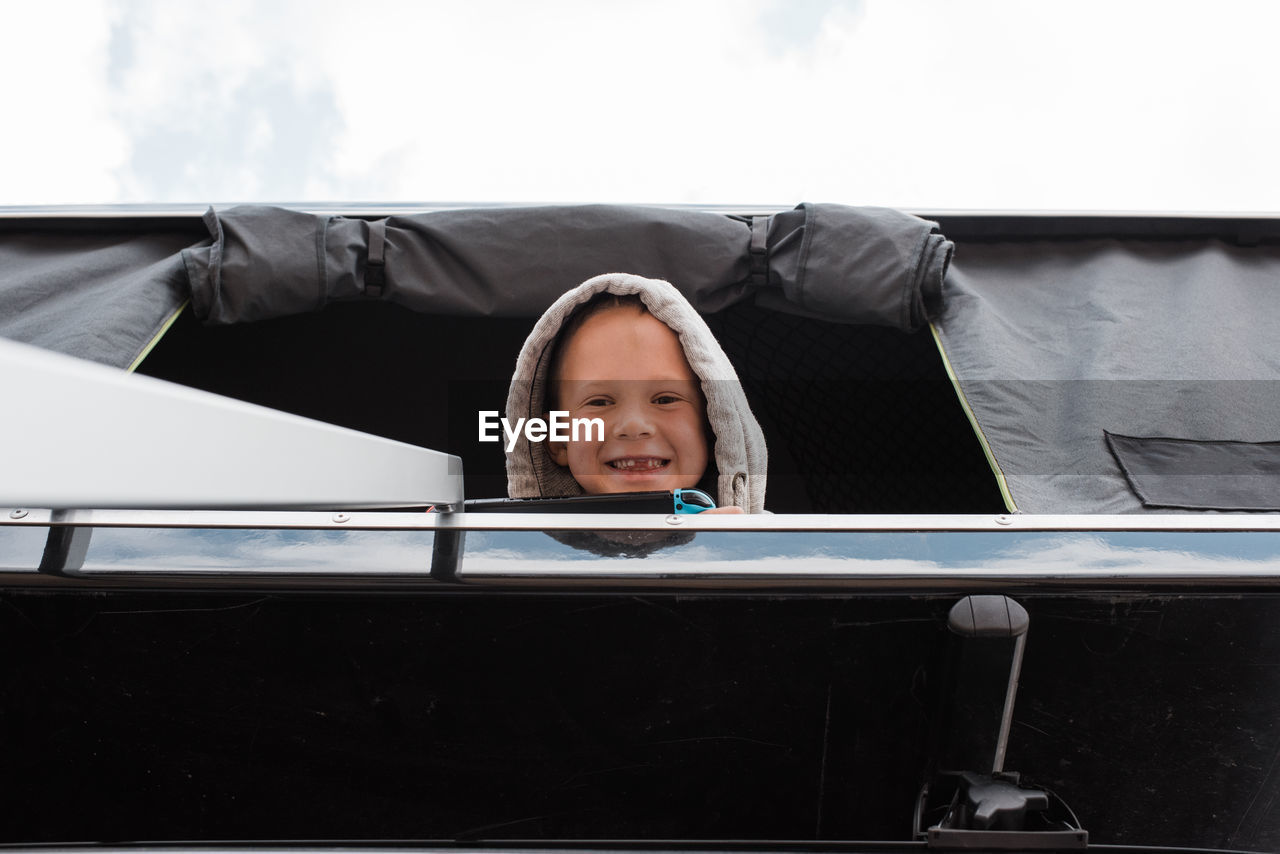 Boy smiling from roof top tent whilst camping