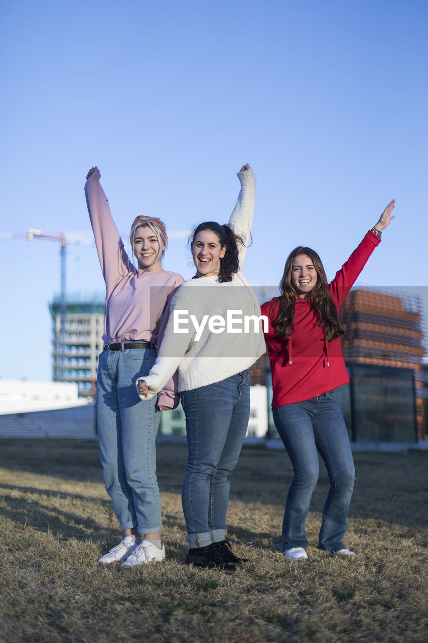 Portrait of smiling friends with hand raised standing in city
