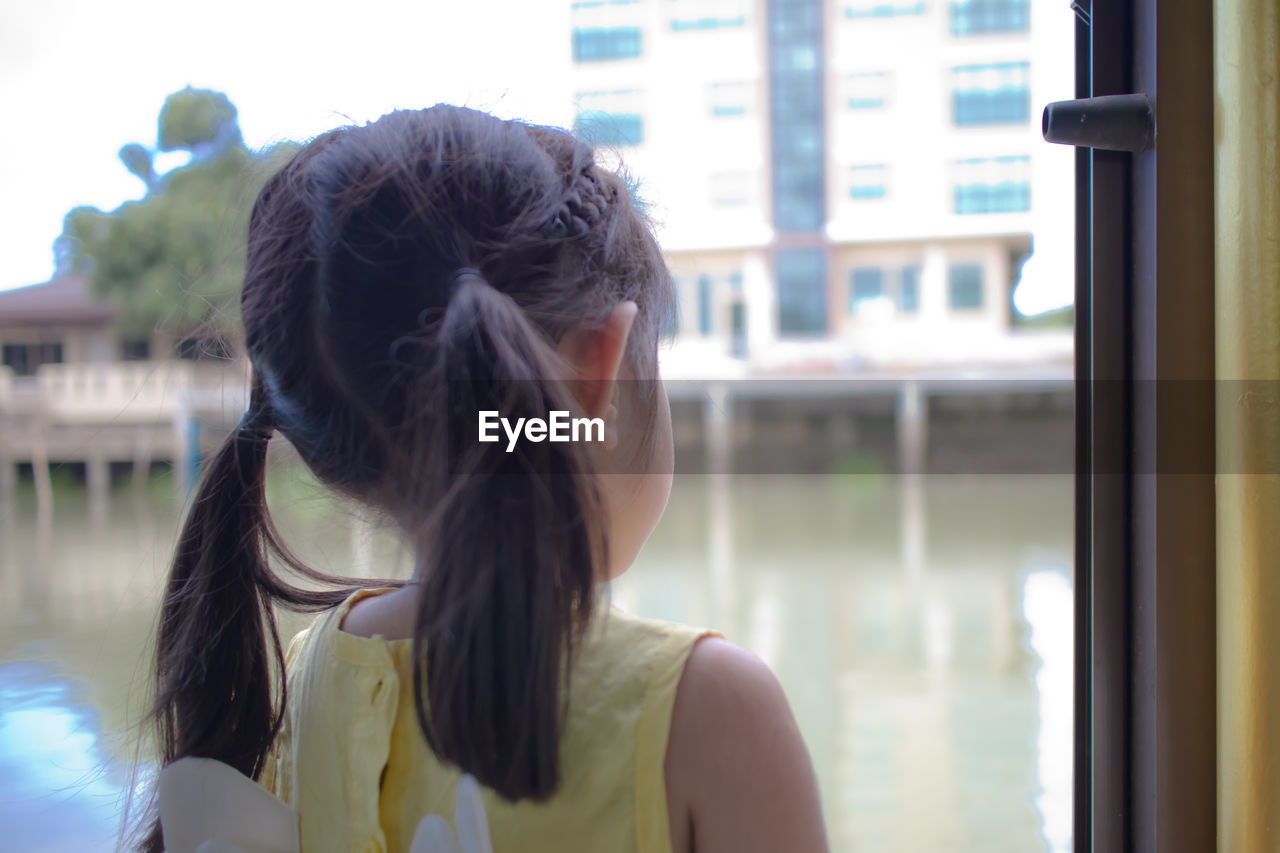 Back view of a little girl looking outdoors through a window