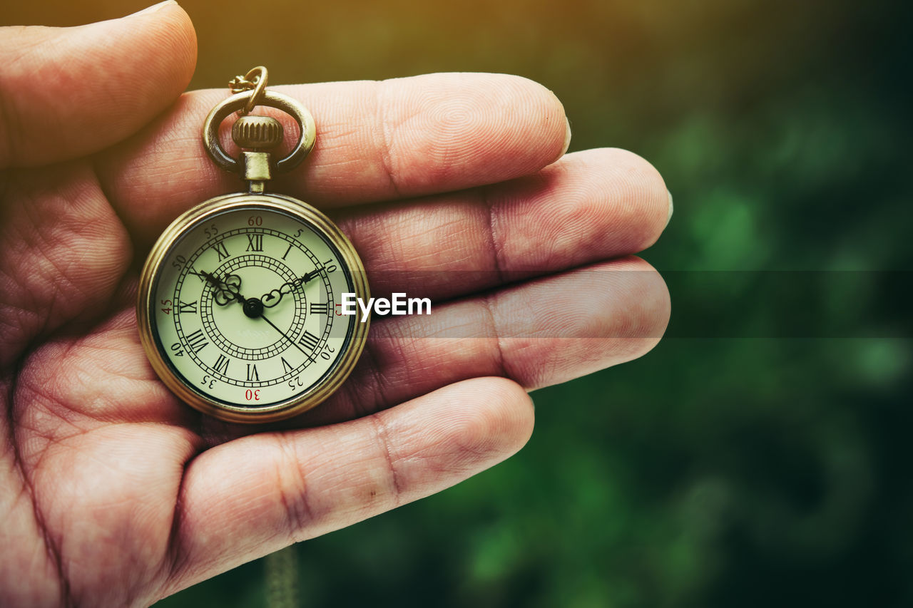 Close-up of hand holding pocket watch outdoors