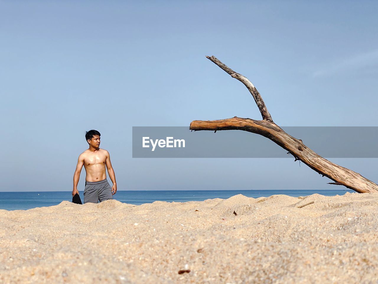 Shirtless man walking at beach against sky