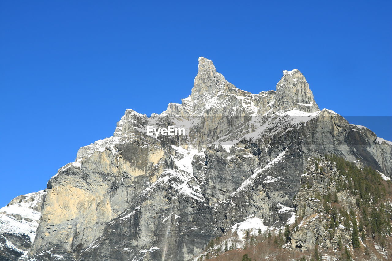 Low angle view of snowcapped mountain peak against clear blue sky